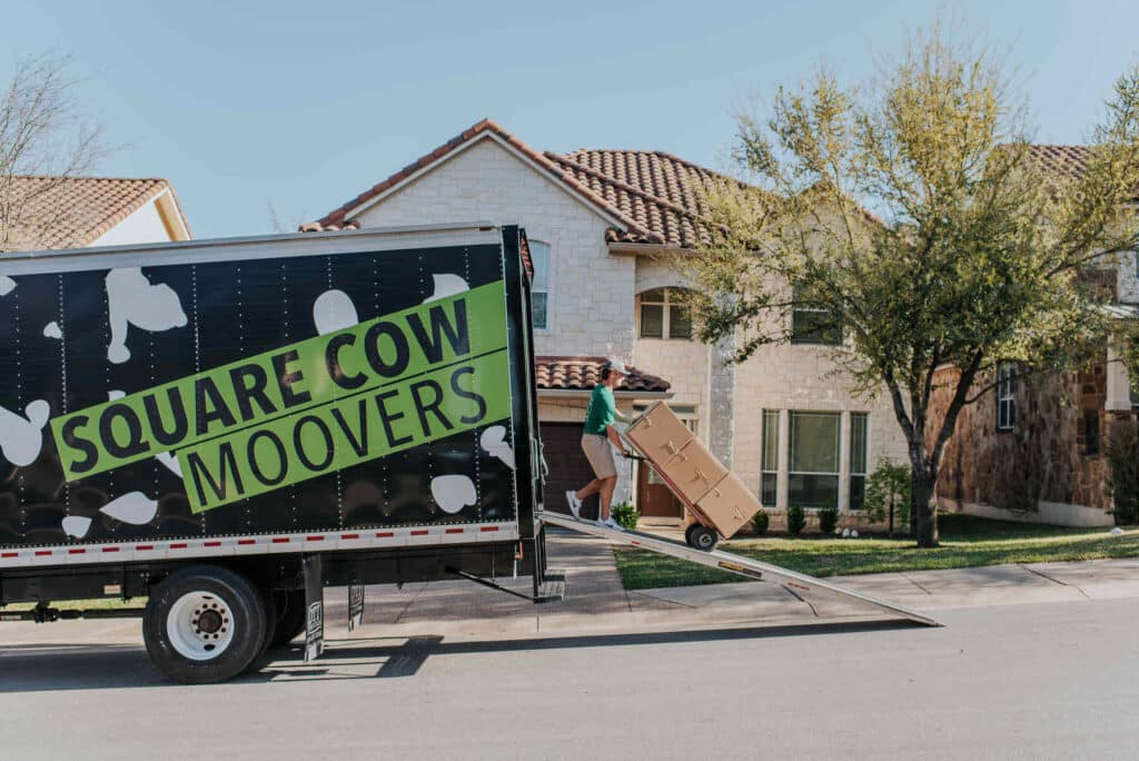 Mover loading a large box onto a Square Cow Movers truck using a ramp