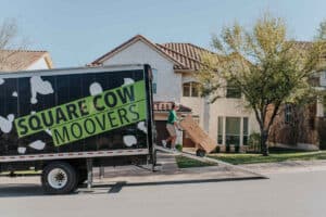 Mover loading a large box onto a Square Cow Movers truck using a ramp