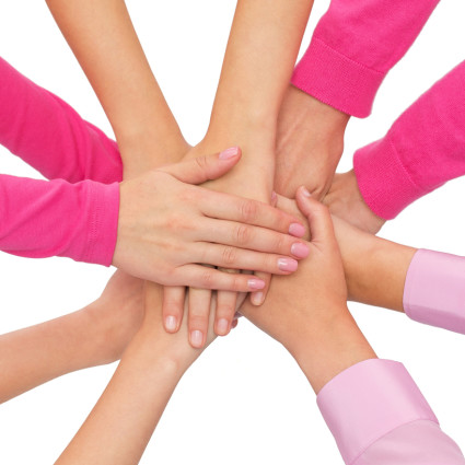 feminism, women power and breast cancer awareness concept - close up of women hands on top of each other over white background