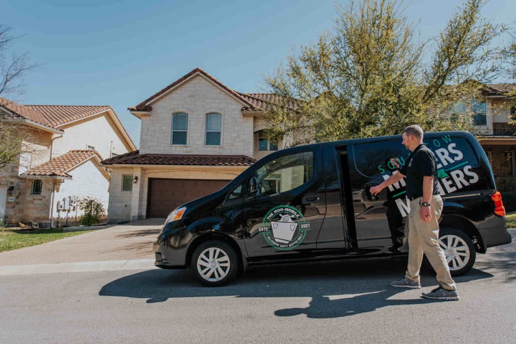Moving company van parked in front of a suburban home with a mover walking nearby