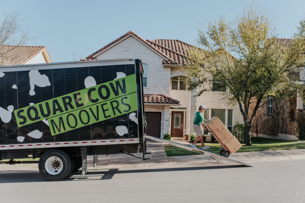 Mover wheeling a large box up a ramp into a moving truck outside a house