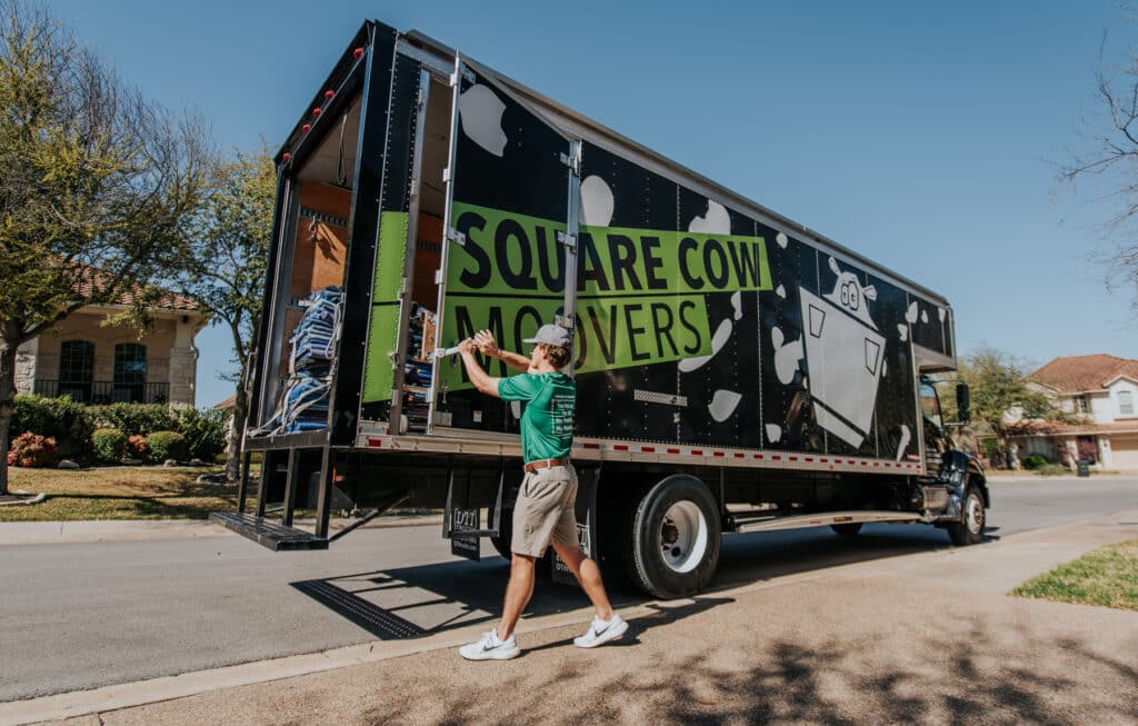Mover closing the back door of a moving truck parked on a residential street