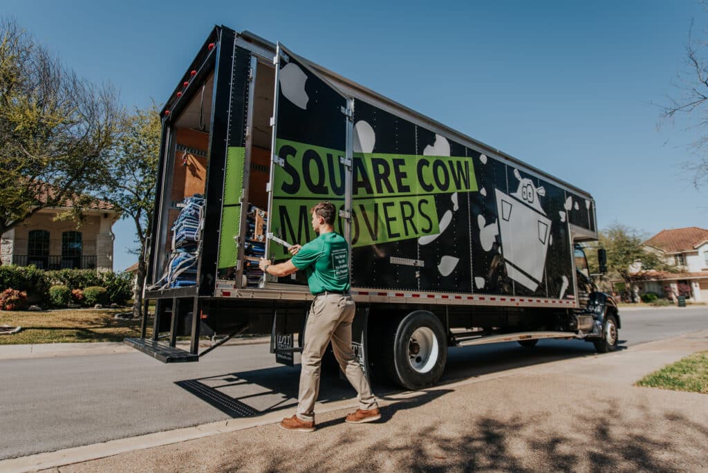 Mover closing the back of a Square Cow Movers truck parked in a residential neighborhood