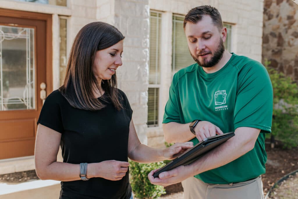 A man and woman stand outside a house, both holding a tablet and looking at it together