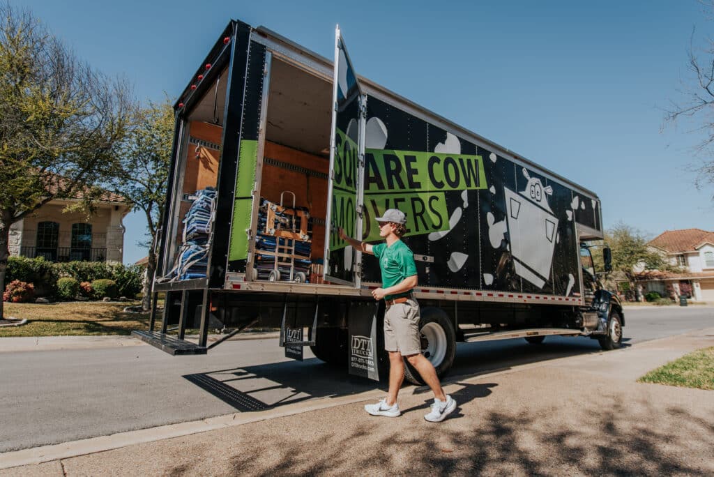 A mover closes the back of a Square Cow Movers truck loaded with supplies