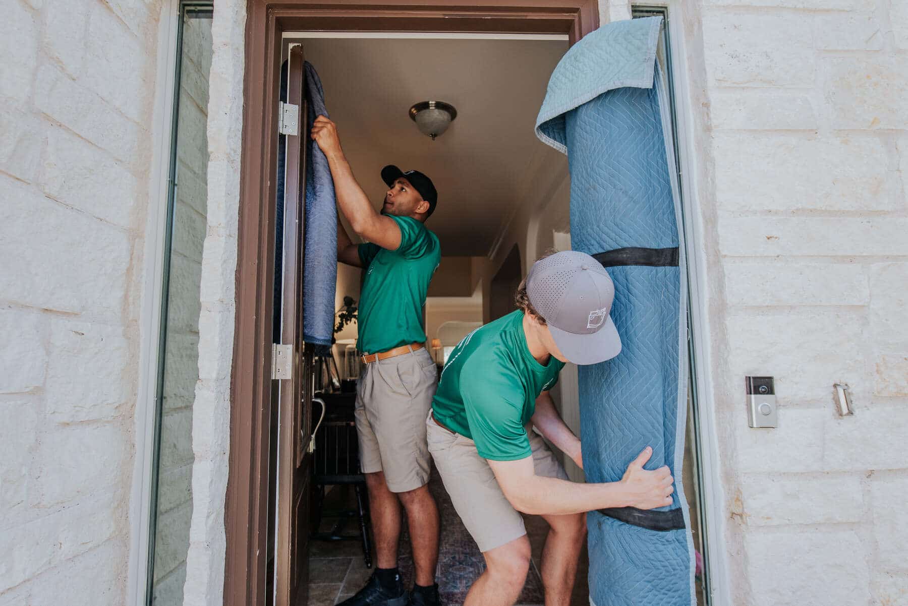 Two men in green shirts are lifting and moving a large piece of fabric together