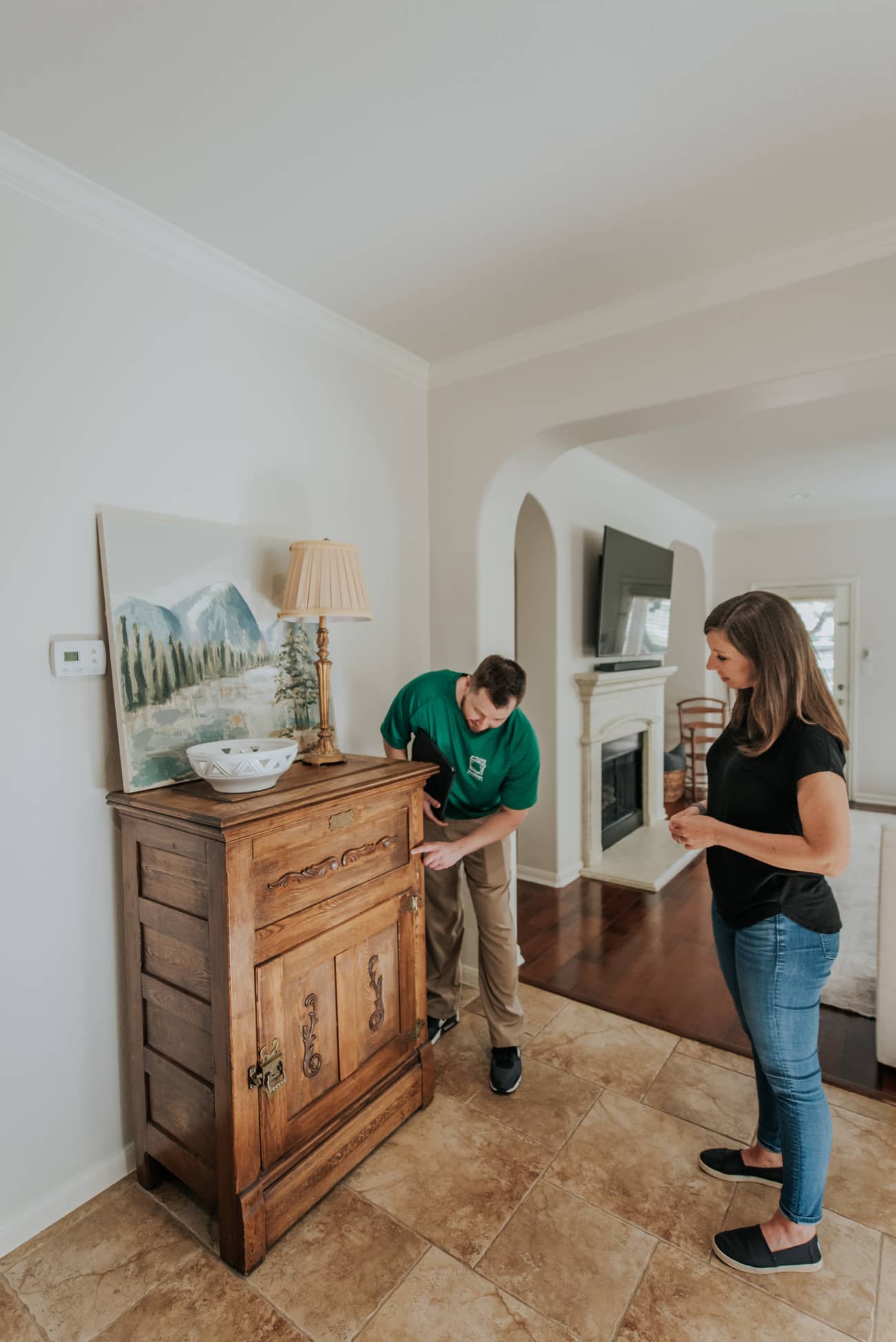 Mover adjusts furniture while a woman observes in a living room