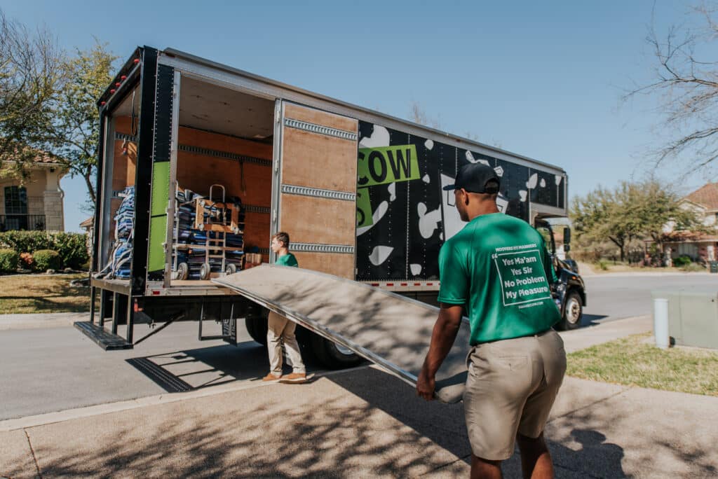 Two movers carrying a heavy wooden dresser down a truck ramp