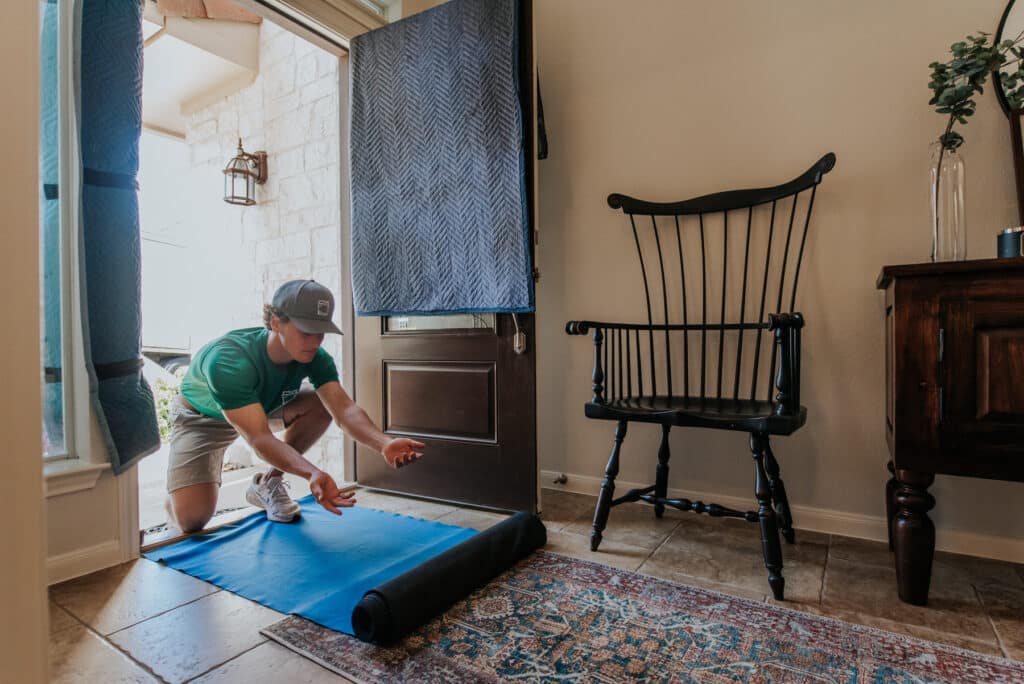 A man lays a blue mat over a patterned rug in a well-lit room