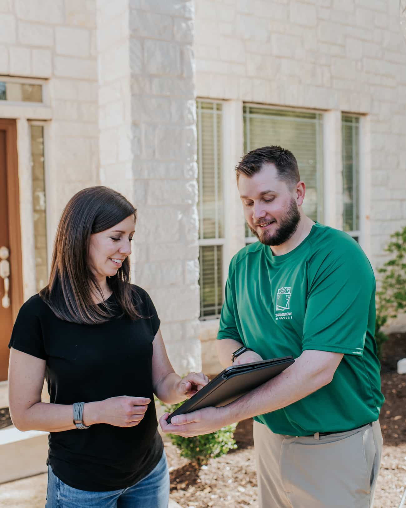 A man and woman stand in front of a house, holding a clipboard and discussing its features
