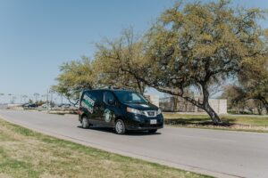 A black Square Cow Moovers van drives down a sunny suburban street.