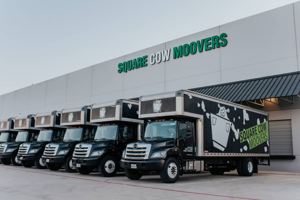 A fleet of Square Cow Movers trucks parked in front of their company building.