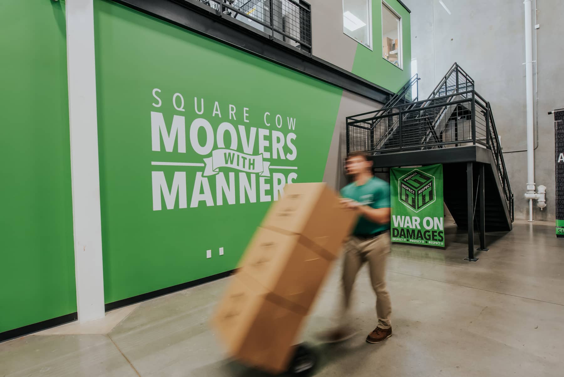 Square Cow Movers employee pushing a dolly with boxes in a warehouse